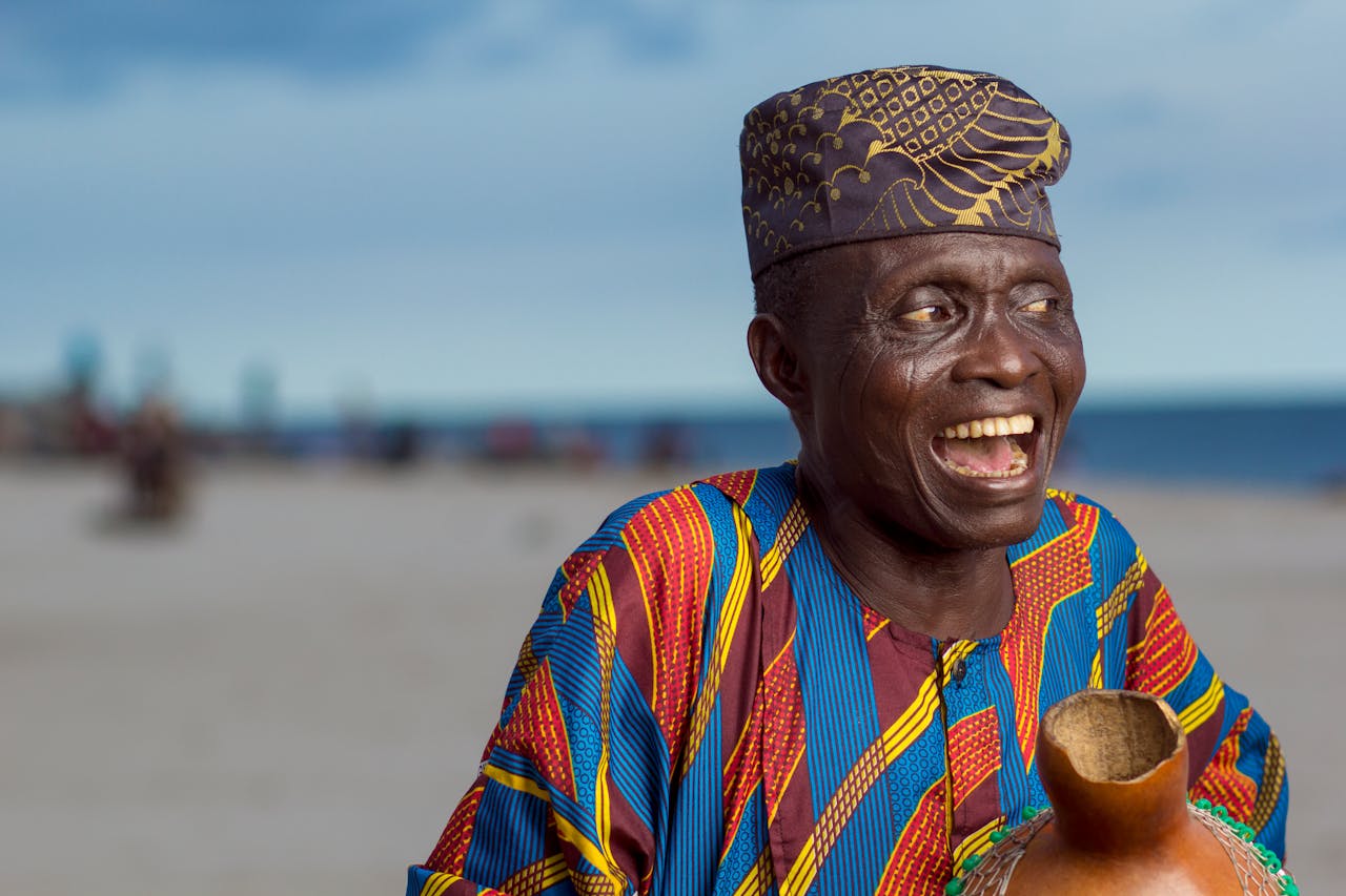 portfolio-02 Elderly man joyfully smiling wearing Yoruba attire and cap on Lagos beach.